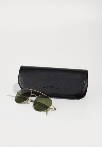 Runda gröna solglasögon med guldmetallram och klara gröna skalmar, placerade bredvid ett svart strukturerat glasögonfodral märkt "Giorgio Armani."