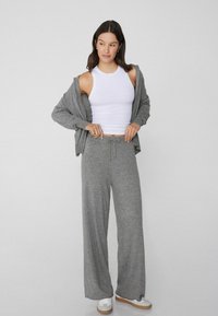 Szary dzianinowy hoodie i szerokie dresy połączone z białą tank top. Materiał wydaje się być miękki, z luźnym krojem i elastycznym pasem ze sznurkiem.