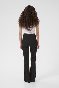 Black flared jeans with a high waist, two back pockets, and a textured fabric. Worn with a white fitted tank top. Viewed from the back.