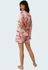 Light pink short-sleeve pajama set featuring a snake pattern in red. Loose fit, soft fabric, with matching shorts and rolled cuffs.