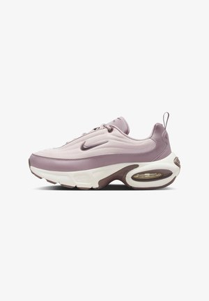 Jasnofioletowy sneaker z teksturowaną siateczką na cholewce, zaokrąglonym designem i brązowymi akcentami. Posiada widoczną poduszkę powietrzną oraz pętlę na pięcie.