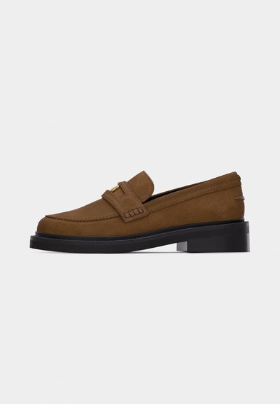 Mocassin en daim marron avec talon bloc noir et détail de boucle dorée sur la tige, présenté en profil latéral sur fond blanc.