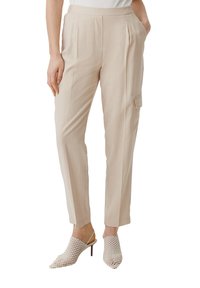 Beżowe spodni z kantem, z kieszeniami bocznymi i małą kieszonką na klapkę. Noszone z teksturowanymi białymi mule na obcasie. Gładki materiał.