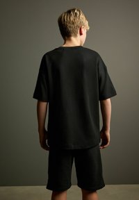 Sort bomuld T-shirt med en afslappet pasform og korte ærmer, parret med matchende sorte shorts. Glat tekstur med et enkelt design.
