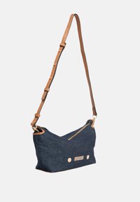 Sac en bandoulière en denim bleu avec fermeture zippée, sangle réglable beige, et accents métalliques décoratifs à l'avant pour plus de détails.
