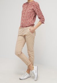 Rød blomsterbluse med krave, lysebeige tapered bukser og hvide sneakers. Blusen har lange ærmer og en afslappet pasform.