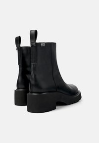 Botines de cuero negro con suela gruesa, que presentan una textura suave, pestañas de tirón y un diseño simple sin adornos.