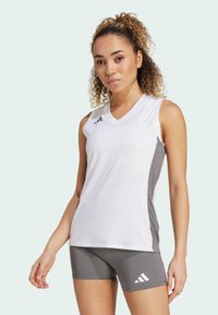 Camiseta atlética sin mangas blanca con paneles laterales grises, diseño de escote en V y detalle de logo de tres franjas. El material parece ligero y suave.