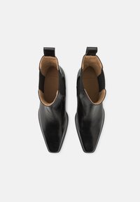 Botines de cuero negro con un diseño elegante, puntera puntiaguda, paneles laterales elásticos y una lengüeta trasera para facilitar su colocación. El interior es de cuero color marrón claro.