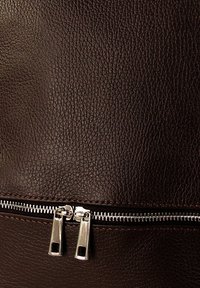 Bruine leren tas met een gestructureerde uitstraling, voorzien van een zichtbare zilveren rits met dubbele trekker, stikseldetails en een gladde, duurzame afwerking.