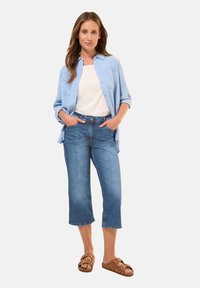 Chemise bleu clair à boutons superposée sur un top blanc, associée à un jean bleu longueur genou et des sandales marron à motifs à pois.