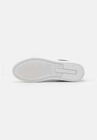 Weißer Sneaker-Sohle aus strukturiertem Gummi mit einem erhöhten Logo in der Mitte. Glatte Außenkanten und leicht erhabene Muster für besseren Halt.
