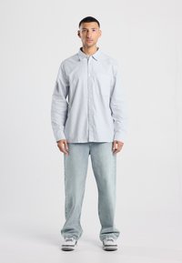 Camicia a righe button-up in blu chiaro e bianco, abbinata a jeans in denim chiaro. Presenta una tasca sul petto e un colletto standard.
