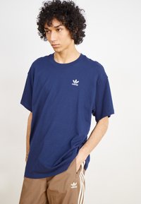 T-shirt en coton bleu marine à manches courtes, col rond, avec le logo Adidas blanc sur la poitrine à gauche ; présente une coupe décontractée.