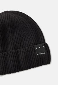 Black ribbed knit beanie featuring a rectangular label with "CPH" and "STUDIOS" in white text. Soft texture and snug fit.