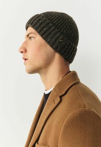 Dark ribbed knit beanie with speckles, worn by a male model with short hair, paired with a brown wool coat. Side profile view.