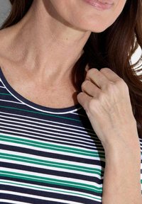 Top rayé bleu marine et blanc avec des accents verts, présentant un col rond et une texture douce, partiellement obstrué par une main.