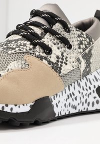 Baskets avec une tige grise et blanche à motif, des accents en daim marron clair contrastants, des lacets noirs et une semelle en caoutchouc texturée.