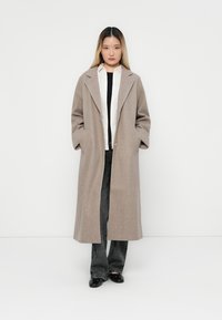Lichtbruin wollen blend jas met een lange, relaxte pasvorm, brede revers en zijzakken, gedragen met een wit shirt en donkere broeken.