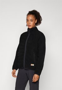 Giacca in pile nera con collo alto, apertura a zip frontale e due tasche laterali. Presenta un tessuto texturizzato e una piccola patch con logo all'orlo.