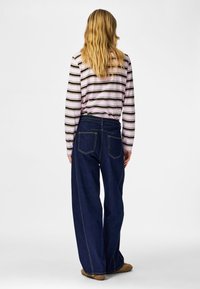 Top de manga larga a rayas en rosa y negro; combinado con vaqueros azul oscuro de corte holgado que tienen dos bolsillos traseros y detalles de costuras visibles.