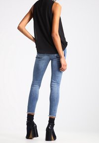 Musta hihaton paita yhdistettynä vaaleansinisiin slim fit -farkkuihin, joissa on rispaantunut helma, ja kuvioituihin nilkkabootseihin, joissa on paksu korko.