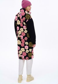 Fleecový kabát s veľkým kvetinovým vzorom v ružovej, žltej a zelenej farbe na čiernom pozadí; obsahuje vysoký golier a štruktúrovanú tkaninu.