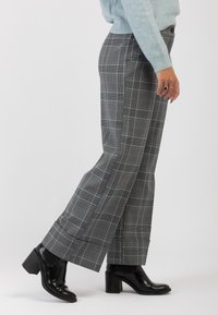 Pantaloni a quadri grigi con gamba larga, caratterizzati da un motivo a scacchi blu chiaro e un tessuto morbido. Abbinati a stivaletti neri con tacco.
