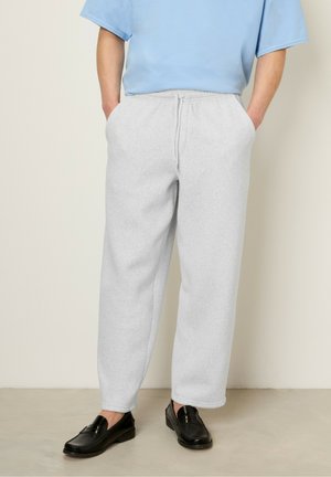 Pantalon de survêtement gris avec une taille élastique et des poches latérales, en tissu doux, associé à une chemise bleu clair et des mocassins noirs.