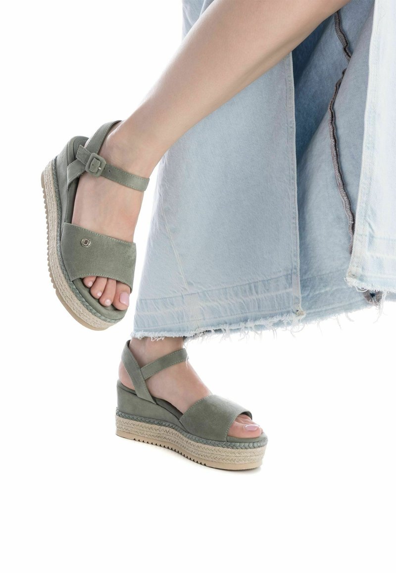 Sandalias de cuña de ante verde con punta cerrada, tira en el tobillo y suela de yute trenzado. El diseño cuenta con una plataforma cómoda y un ligero tacón.