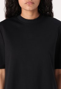 T-shirt en coton noir avec col rond et manches courtes. Le tissu est doux avec une légère élasticité, offrant un ajustement décontracté.