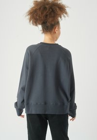 Felpa grigia scura con vestibilità comoda, maniche raglan e una texture morbida. L'orlo e i polsini sono a costine, offrendo una finitura confortevole.