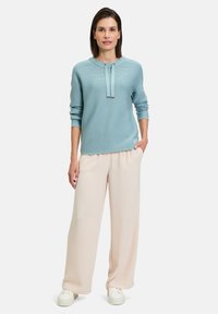 Pull bleu clair côtelé avec un col rond, des manches longues et des détails à cordon, associé à un pantalon crème ample et des baskets blanches.