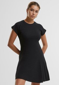 Robe noire à manches courtes avec un corsage ajusté et une jupe évasée. Texture côtelée, col rond et détails de couture subtils.