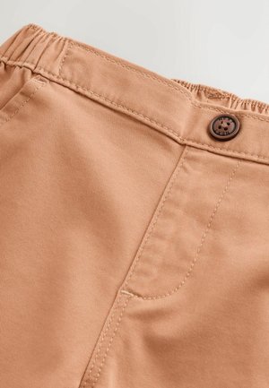 Vaaleanruskeat joustavyötäröiset housut, joissa on teksturoitu kangas. Housuissa on pyöreä ruskea nappi ja vasemmalla puolella sivutasku.