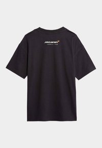 Svart bomull T-shirt med korta ärmar och rundad halsringning. Bakom finns McLaren-logotypen i vitt med en orange accent.