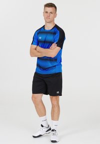 Blå och svart atletisk tröja med horisontella ränder, ihop med svarta shorts. Har logotyp på tröjan och vänster shortben. Vita sportskor.