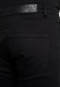 Vaqueros de mezclilla negra con un bolsillo trasero visible, etiqueta de cuero con "GABBA" y un acabado de tela suave y texturizado.