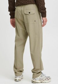 Beige tapered pants with an elastic waistband, back pocket with button, and double side pockets; worn with gray and white athletic shoes.
