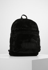 Sac à dos noir en fausse fourrure douce, avec un logo en relief prominent, une forme arrondie, une poignée supérieure et des poches à double zip.