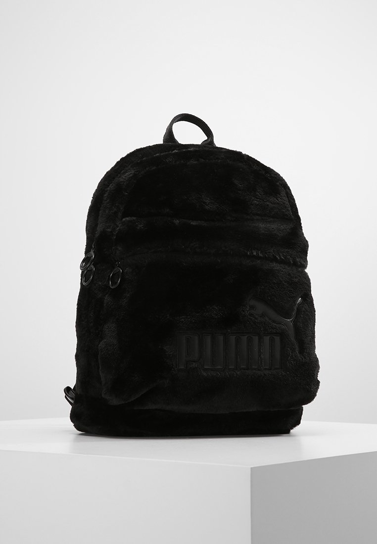 Sac à dos noir en fausse fourrure douce, avec un logo en relief prominent, une forme arrondie, une poignée supérieure et des poches à double zip.
