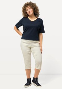 Marineblauwe T-shirt met korte mouwen en V-hals met oranje bies, gecombineerd met lichtbeige cropped broek. Model draagt zwarte high-top sneakers.