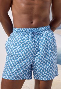 Bañador azul con un estampado de huellas de manos blancas, cinturilla elástica con cordón ajustable y tejido ligero.