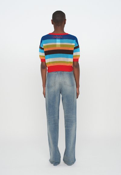Knit top with multicolored stripes, featuring a red hem, paired with light blue flared jeans, seen from the back against a white background.