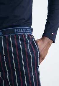 Mørkeblå pyjamashorts med vandrette striber i hvid og rød, featuring en blå elastisk talje med "HILFIGER" branding.