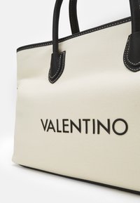 Tygväska i krämfärgad med svarta läderdetaljer. Har sömnadsdetaljer och "VALENTINO"-logotyp i fet, svart text.