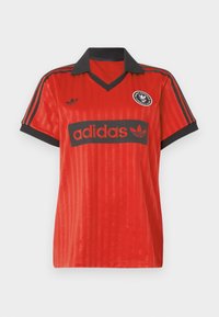 Raudona Adidas futbolo marškiniai su juodu apykaklės kraštu, juodais rankogaliais, juodomis juostomis ant pečių ir Adidas logotipais ant krūtinės bei kairėje pusėje.