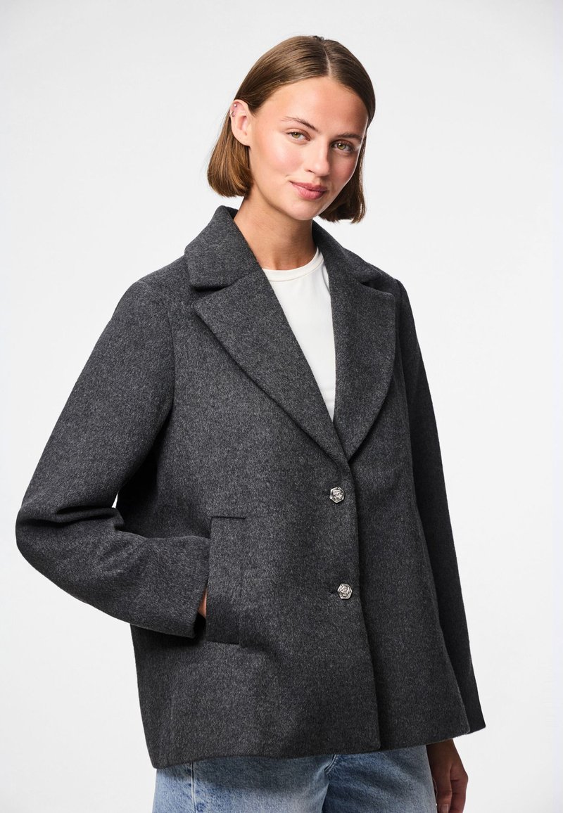 Grå ullblandad kappa med slagkrage, två framfickor och knappstängning. Har en lös passform och textilstruktur.