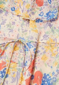 Tissu léger avec un imprimé floral multicolore comprenant des fleurs jaunes, violettes, bleues, vertes et rouges, noué avec un fin ruban en tissu.