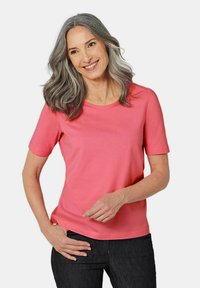 Kurzärmliges, rundhalsiges T-Shirt aus leuchtend rosa Baumwolle mit glatter Textur und lockerer Passform, kombiniert mit dunklen Jeans.